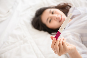 Selective focus Pregnancy test positive result on hand of smiling woman in her bedroom.