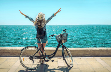 Blonde woman in summer hat with her bicycle walking coastline by