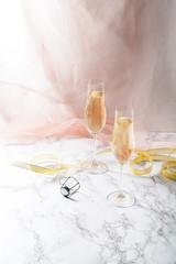 Obraz na płótnie Canvas Two flute glasses with champagne on marble background. Pink transparent fabric. Soft light