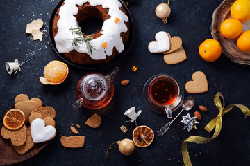 Fototapeta na wymiar Traditional christmas cake with dried fruits soaked in rum and sugar glaze. Teatime with heart-shaped ginger cookies. Christmas background with festive decoration. Horizontal composition