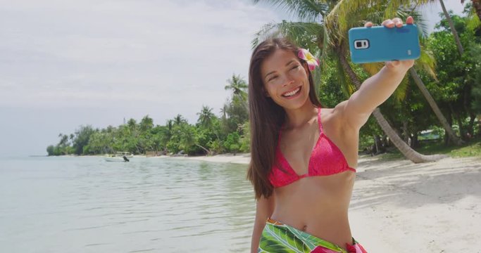 Woman taking smart phone selfie video or photo- Bikini travel girl on beach smiling happy on Matira Beach, Bora Bora. Joyful girl on holidays beach vacation wearing bikini in Tahiti, French Polynesia.