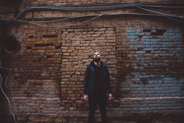 Fototapeta na wymiar Modern young bearded man in black style clothes posing against brick wall.