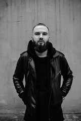 Modern young bearded man in black style clothes standing in urban background.