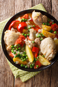 Pieces of chicken stew with potatoes, peppers, tomatoes, peas and onions close-up. Vertical top view