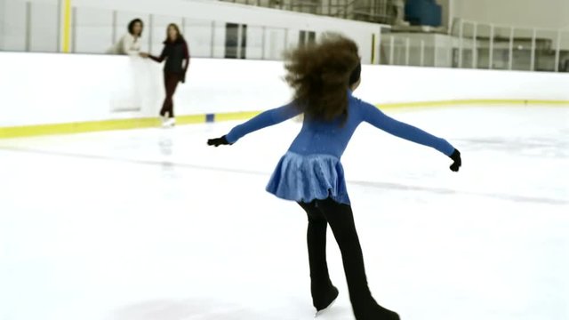 Little African girl in ice dancing costume skating on indoors rink with arms outstretched