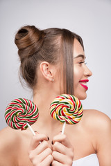 Naklejka premium Beauty fashion model with colourful lollipops. Young pretty woman with pink lips and makeup. Candies like a sunglasses