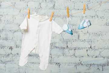 Children's white body and blue shoes on a rope against a white brick wall.