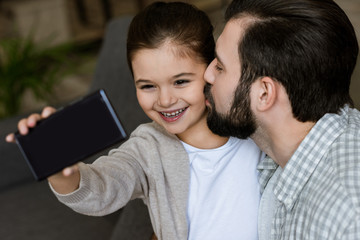 cheerful father with daughter taking selfie on smartphone at home