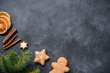 Christmas background with fir tree branches, cinnamon, gingerbread cookies and dried orange rings. Dark stone or textured chalkboard background. Copy space for text