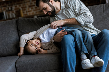 Fototapeta premium father with daughter laying on couch, hugging and laughing at home