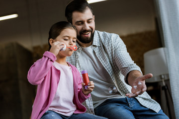 happy father with daughter blowing bubbles at home