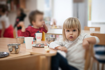 Obraz na płótnie Canvas Little caucasian girl having breakfast in kindergarten, portrait looking at camera