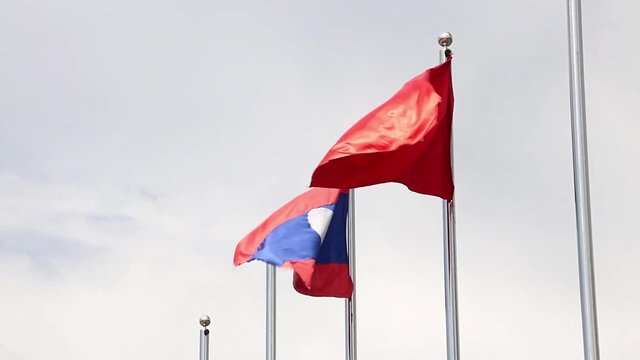 Lao National Flag with red flag with communist symbols of a sickle with a hammer flying in a blue sky, Laos