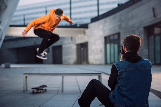 man taking photo of skateboarder jumping over bench