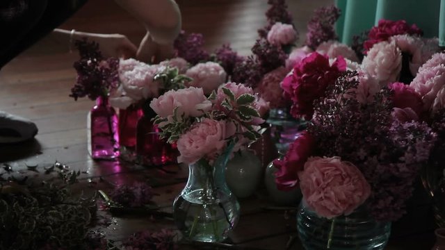Florist cuts flowers and puts them in containers with water on floor. Woman complements pink flowers in different vases with green stems, which shears with scissors.