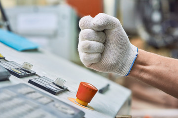 Side view close up of male hand in working glove pressing big red STOP button in case of safety...