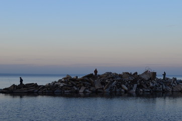 a small island of construction debris, stones and concrete in the sea and fishermen on it