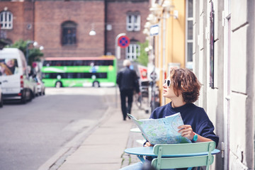 Young beautiful female traveler sits in cafe on the street and looking at the map