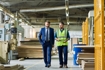 Full length portrait of young workman giving tour of modern factory to handsome mature businessman...