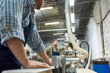 Side view portrait of two men wearing in overalls working in factory shop operating modern machines, copy space