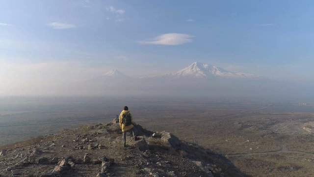 Aero shot: backpacking extreme expedition at Armenia. Aerovideo: unmanned aircraft flying above wonderful natural peaceful area where one hike man in colorful jacket look at panorama of snowy peaks