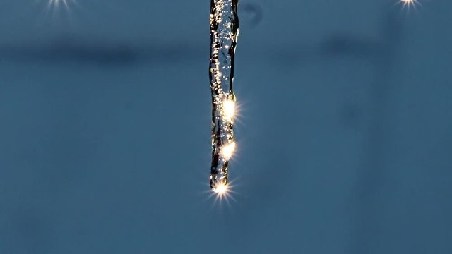 The icicle is glitter in the sun, a close up. Water drops falls from an icicle with a stars reflection of the sun. Sparkle of icicle.