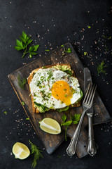 toast with avocado, spinach and fried egg on wooden cutting board, black background