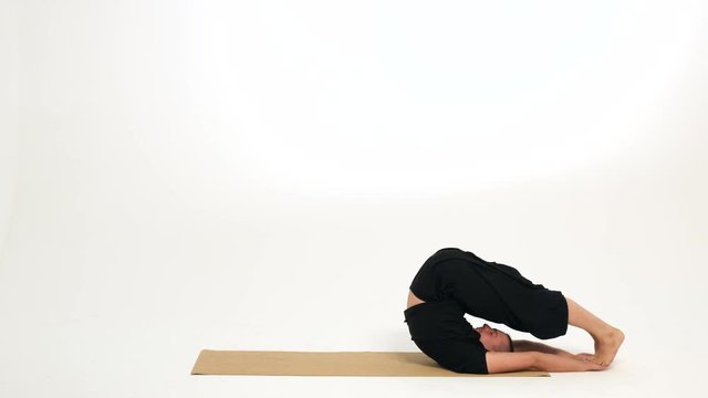 Man demonstrates plow pose  and crab pose/table top pose on a yoga mat against a white background.