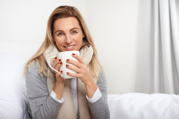 Attraktive blonde Frau mit einem Becher lächelt in die Kamera