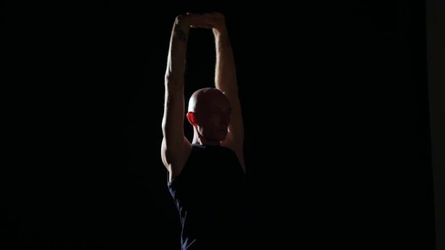 Silhouette of a man stretching in a darkened room. He is stretching his arms and rotating his upper body.