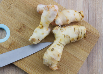 Fresh galangal fresh herbs on a cutting board with knife on wood table background.