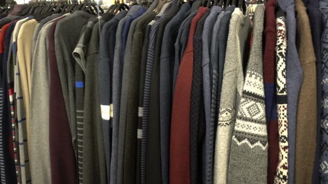 Fashionable collection of warm clothes. Various sweaters hang on hangers on the rack. HD video clip