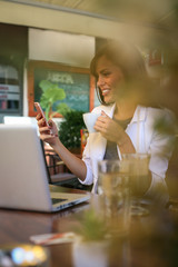 Young woman drinking coffee, using phone.