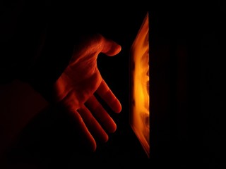 man's hand in front of a burning pellet stove.