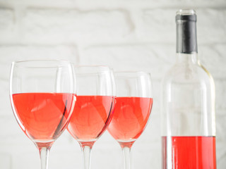 Three wineglass with pink wine and bottle on white brick wall background