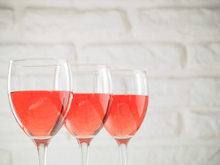 Three wineglass with pink wine on white brick wall background