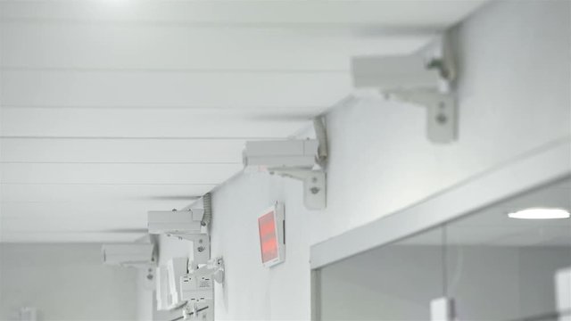 Surveillance cameras hang in the office building on the white wall.