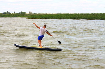 Stand up paddle surfer turns over (drop out) from Stand up paddle board (SUP) into green water of stormy lake