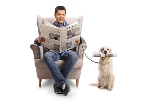 Young man seated in an armchair holding a newspaper and a labrador retriever with a newspaper