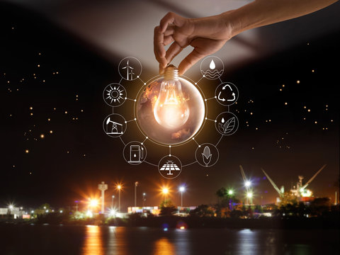 Hand holding light bulb in front of global show the world's consumption with icons energy sources for renewable, sustainable development. Ecology concept. Elements of this image furnished by NASA.