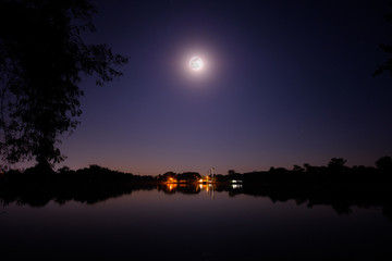 Full moon shine bright in the night above the big lake and small village