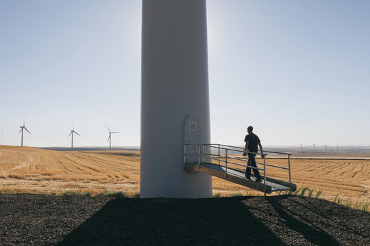 A wind farm technician standing and using a laptop at the base of a turbine on a wind farm in open countryside at Palouse. 