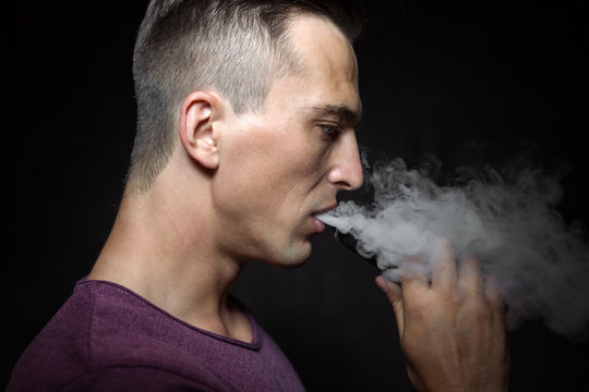 Man on black background vaping and releasing a cloud.