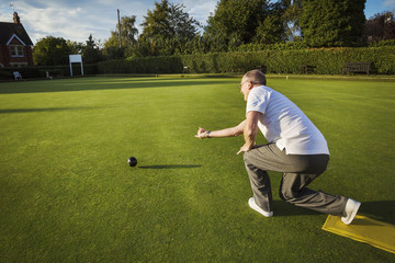 A lawn bowls player standing on a small yellow mat preparing to deliver a bowl down the green, the smooth grass playing surface. 