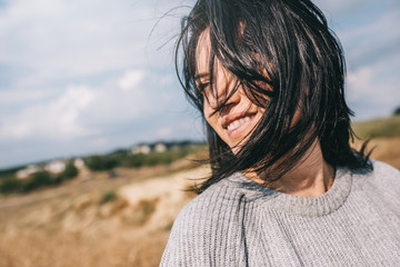 Horizontal cropped portrait of beautiful smiling woman wearing sweater being playful with windy...