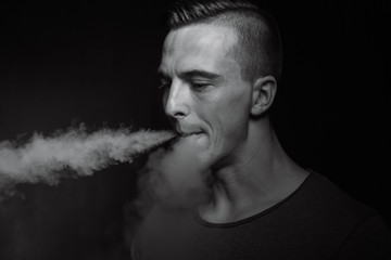 Men on black background vaping and releases a cloud of vapor.