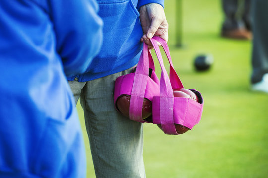 Two people in blue shirts, one carrying four wooden lawn bowls in a pink bag. 