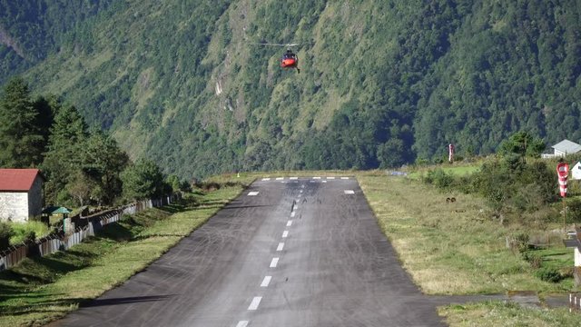 Landing of a red helicopter in Lukla TenzingHillary Airport. Helicopters are used for transporation of tourists and stuff to the base camps in the Himalaya