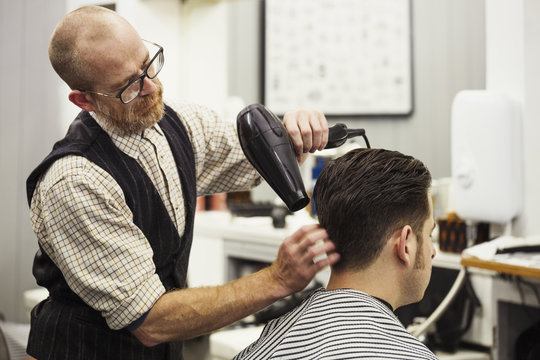 A customer sitting in the barber's chair, having his hair blow dried by a hairdresser and barber. 