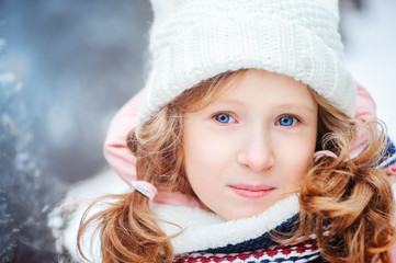 winter portrait of 8 years old kid girl walking outdoor in snowy day, wearing white knitted hat and pink coat